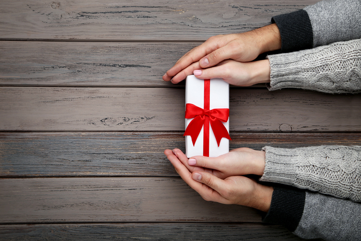 Female and male hand holding gift box on grey background